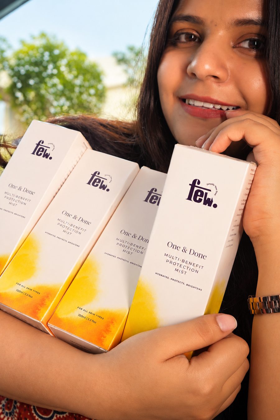 A woman smiling and holding four boxes of FEW One & Done
